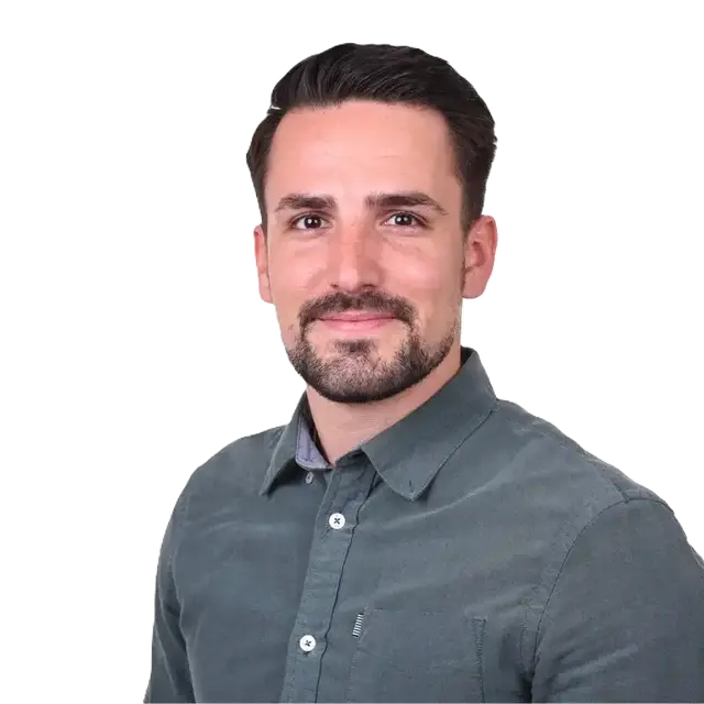 Mann mit Bart lächelt in die Kamera trägt ein dunkelgraues Hemd vor weissem Hintergrund