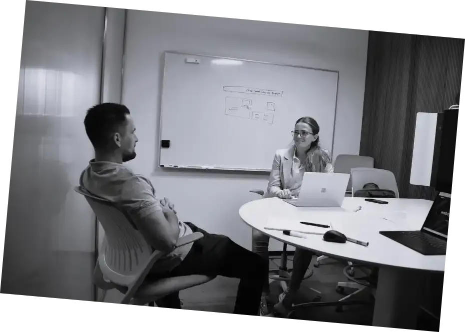 Schwarzweissbild von zwei Personen im Besprechungsraum mit Whiteboard im Hintergrund.